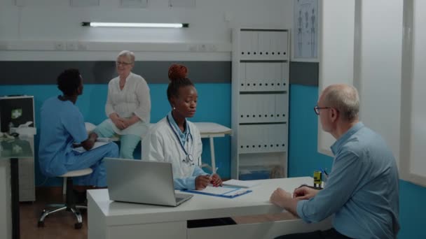 Lekarz konsultujący starszego pacjenta z chorobą w gabinecie lekarskim - Materiał filmowy, wideo