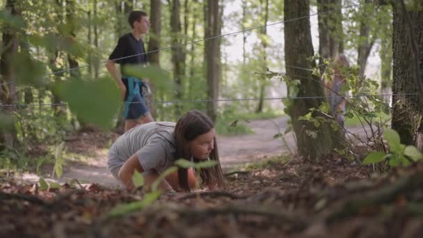 Los niños en un campamento de verano caminata se arrastra en el suelo. Entrenamiento de obstáculos que pasan arrastrándose en el suelo. Una chica cae en el bosque en una misión de campamento - Imágenes, Vídeo