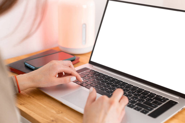 Kaukasische Frau arbeitet am Laptop, tippt auf der Tastatur und blickt auf den weißen leeren Bildschirm. Auf dem Holztisch Laptop, Notizblock und Handy. Freiberufler, die vom Homeoffice aus arbeiten. Kopierraum. - Foto, Bild