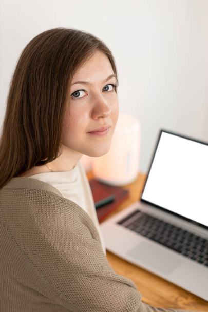 Calm caucasian woman tired of working at computer. Working from home office. Attractive brunette woman looking into camera. Selective focus. On the background empty blank white screen. - Photo, Image