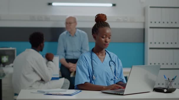 Retrato de la enfermera escribiendo en el teclado del ordenador portátil en la oficina médica - Metraje, vídeo
