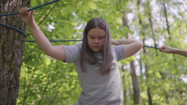 Aktywne dziecko nieustraszenie wspina się po linie między drzewami. Dziewczyna w parku przygody są przeszkodami na drodze linowej. obóz dla dzieci, obóz letni, - Materiał filmowy, wideo