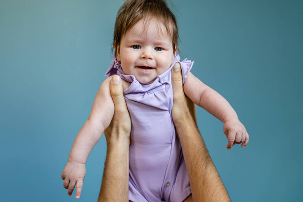 Руки невідомого чоловіка батько тримає свою доньку-дитину в повітрі проти блакитної стіни дитини в фіолетовій сукні в літній день батьківства та батьківства концепція зростає копіювати простір
 - Фото, зображення