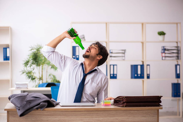 Empleado joven adicto al alcohol sentado en la oficina - Foto, imagen
