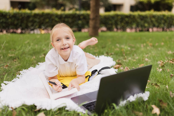 happy caucasian kid has online lesson on laptop during coronavirus covid-19 pandemic and lockdown - Fotó, kép