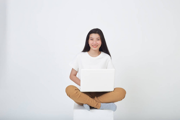 Умная привлекательная молодая женщина использует ноутбук сидя скрестив ноги на сером фоне студии - Фото, изображение