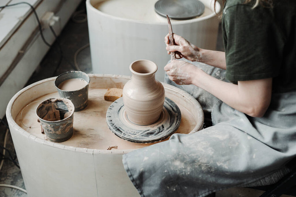 vrouw in groen shirt maken van een klei pot met behulp van het pottenbakkerswiel. het maken van een kalf pot - Foto, afbeelding
