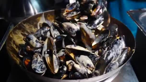 Street food mussels and shells. Cooking and mixing seafood in with spicy sauce large pan. Sale street food on local market or festival. Mediterranean cuisine. Frying on large roasting pan, boiling - Footage, Video