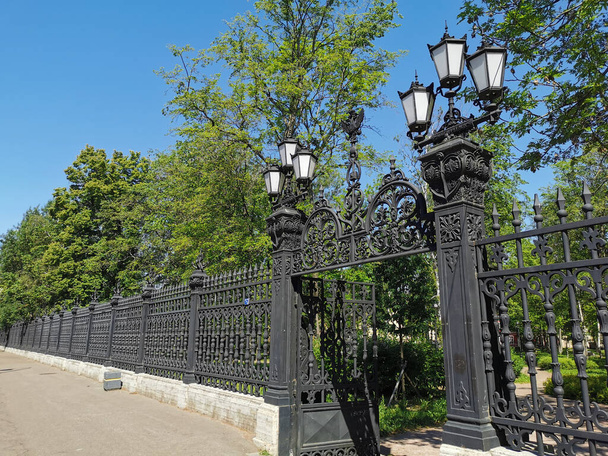 Schöne gusseiserne Tore mit Laternen und einem verzierten Gitter am Eingang zum Sommergarten der Stadt Kronstadt vor dem Hintergrund eines blauen wolkenlosen Himmels. - Foto, Bild
