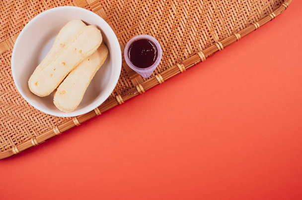 A high angle shot of a bowl of cookies and jam on a woven fabric on a red surface - Fotó, kép