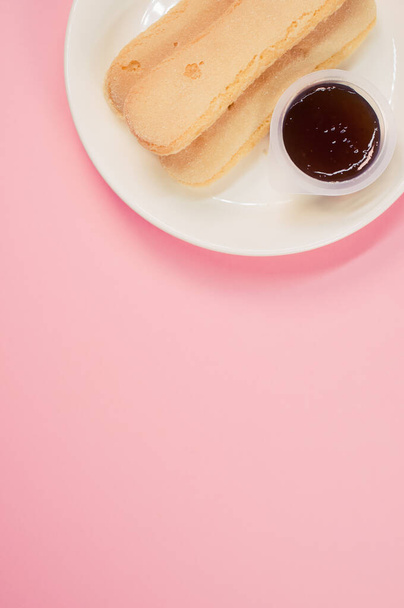 A vertical shot of a plate of cookies and jam on a pink surface - Фото, зображення