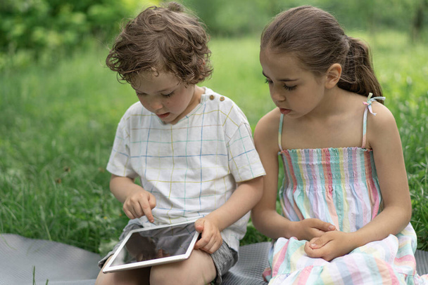 Gyerekek egy tablettával a szabadban. A gyerekek a tableten játszanak. Technológiai koncepció. - Fotó, kép