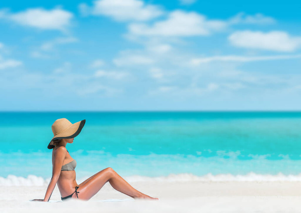 Beach woman sun tanning sunbathing lying down on beach towel in sand body skincare sun exposure protection with hat for skin cancer. - Фото, зображення