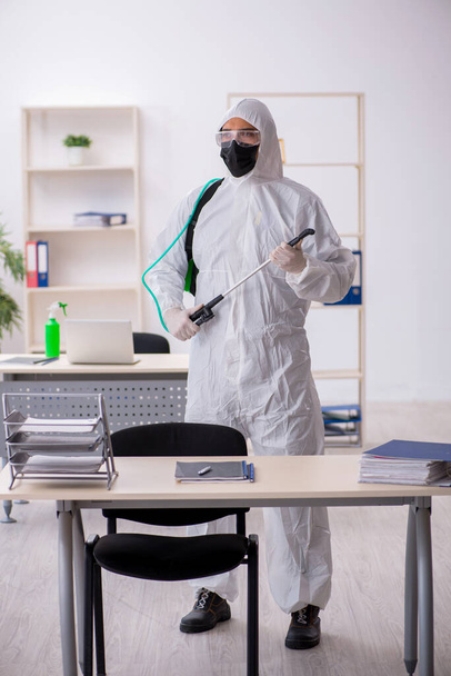 Young male contractor disinfecting office during pandemic - Foto, imagen