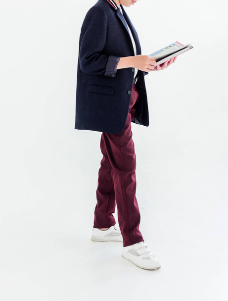 Photo of A schoolboy stands on a white background in a school uniform - trousers, a jacket and a shirt. A boy holding an open textbook in his hands - Foto, Imagen