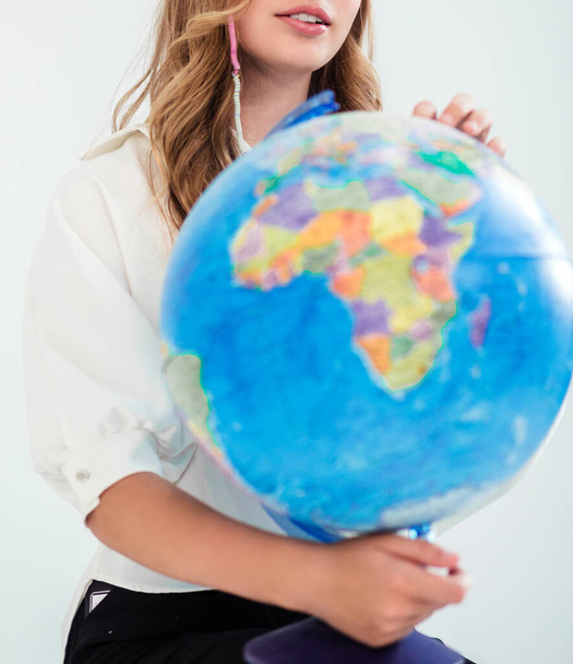 Une fille en chemisier blanc tient un globe dans ses mains et le regarde. Photographie - Photo, image