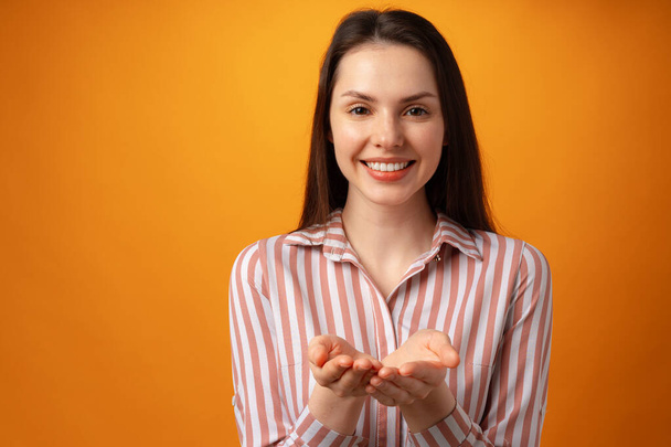 Woman showing something and offering against yellow background - Foto, Imagen