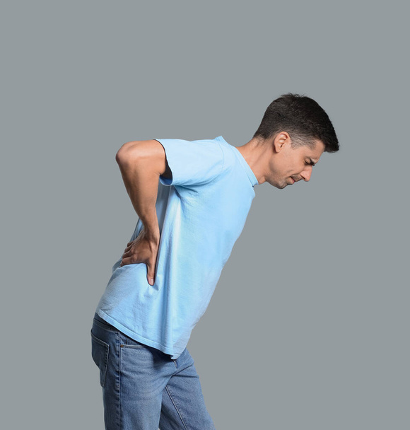 Jongeman die lijdt aan rugpijn op grijze achtergrond - Foto, afbeelding