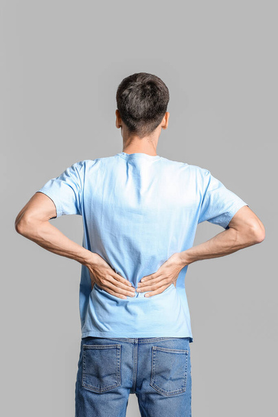 Young man suffering from back pain on grey background - 写真・画像
