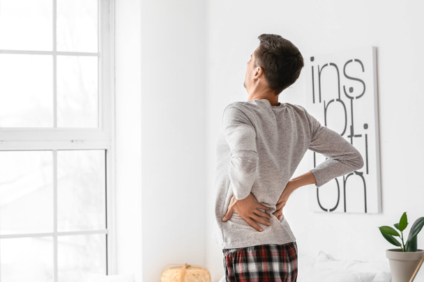 Young man suffering from back pain in bedroom - Photo, Image