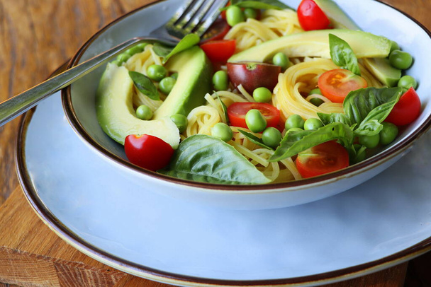 Pasta salad with green peas, avocado, cherry tomatoes and basil on rustic wooden background. Top view. - Photo, image