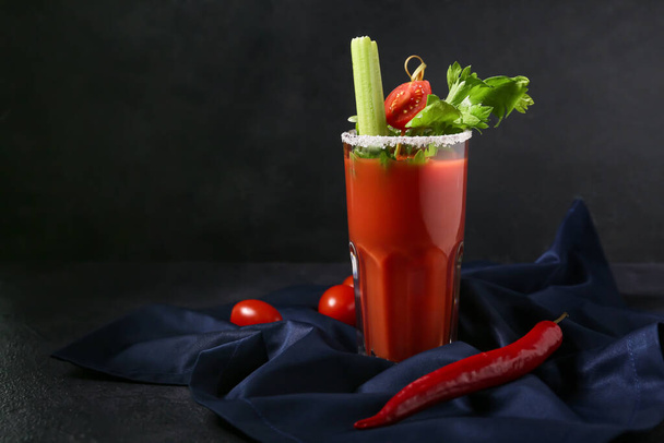 Glass of bloody mary cocktail garnished with celery, cilantro and red chili pepper on dark background - Photo, Image