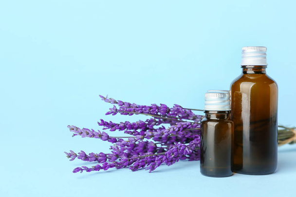 Flaschen mit ätherischem Lavendelöl und Blumen auf farbigem Hintergrund - Foto, Bild