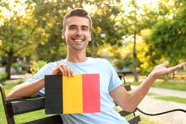 Młody człowiek z flagą Belgii siedzi na ławce na zewnątrz - Zdjęcie, obraz