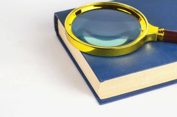 Vergrootglas en blauw gesloten boek in hardcover. Minimalistische compositie op een witte achtergrond. - Foto, afbeelding