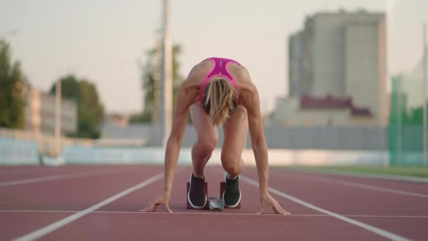 Jedna mladá žena běžec na slunci na stadionu aréně se připravuje na běh dostane do běžeckých bot a běží sprint z startovní čáry ve zpomaleném filmu - Záběry, video
