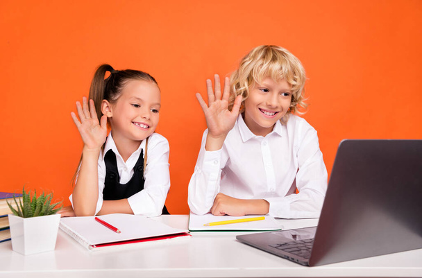 Photo of positive kids distance lesson look netbook wave hand wear uniform isolated orange color background - Foto, Bild