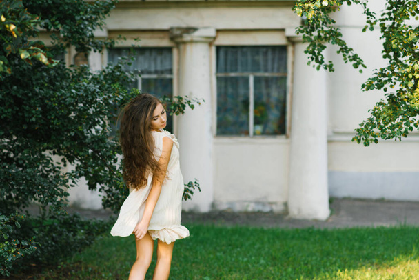 Una joven con el pelo largo corre a través de la hierba en el parque de la ciudad en verano, su pelo revoloteando en el viento. - Foto, Imagen