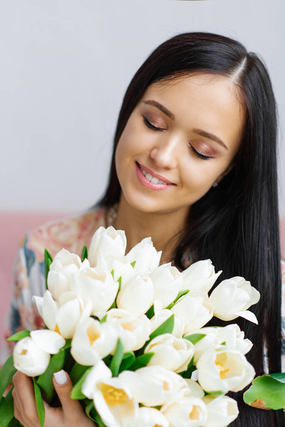 Atractiva morena sosteniendo tulipanes blancos con hermoso maquillaje de cerca - Foto, imagen