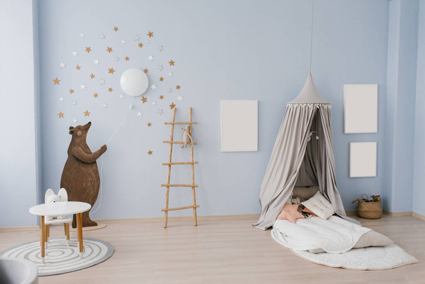 Інтер'єр дитячої кімнати оформлений в синьо-бежевих тонах. Ведмідь тримає маленьку кулю в руках. Ковзання з басейном з пластикових кульок. Наметне ліжко з подушками та іграшками
 - Фото, зображення