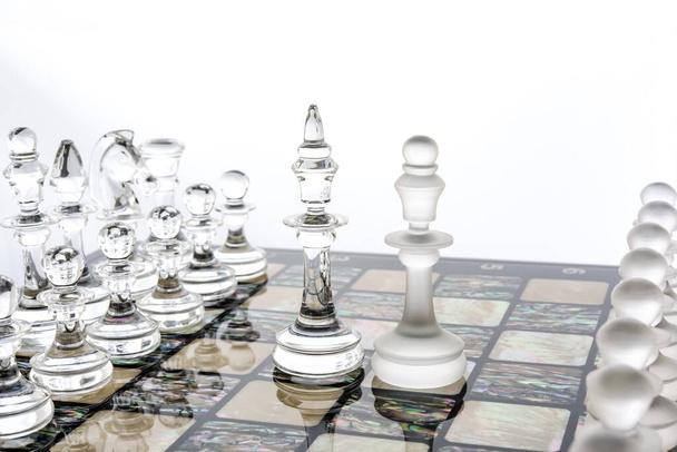 Peças de xadrez de vidro diferentes transparentes figuras em pé sobre placa de pérola em branco. Conjunto de formas brilhante e fosco. conceito de jogo de confrontação. - Foto, Imagem