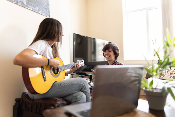 Привлекательная молодая женщина играет на гитаре, пока ее подруга слушает ее музыку. - Фото, изображение