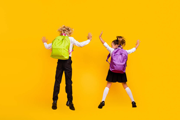 Rear back view photo of funny positive kids jump wear backpack school uniform isolated yellow color background - Foto, afbeelding