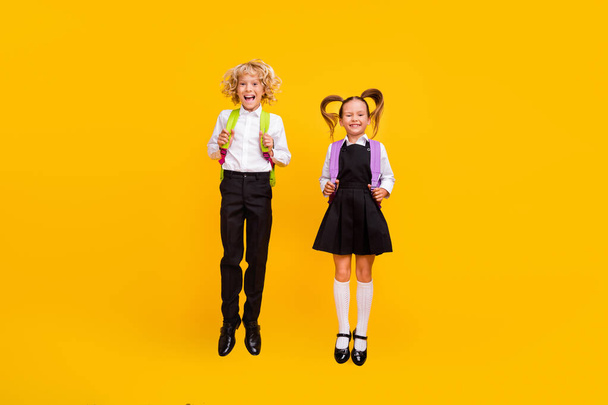 Photo of cheerful excited children jump have fun wear backpack school uniform isolated yellow color background - Фото, зображення