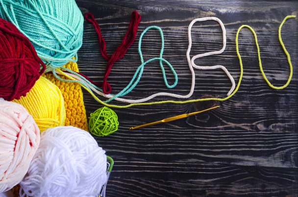 Balls of colored yarn on a fabric background and the word "Yarn" of colored threads on a wooden background of the needlework concept. Balls of colored yarn on a dark background - 写真・画像