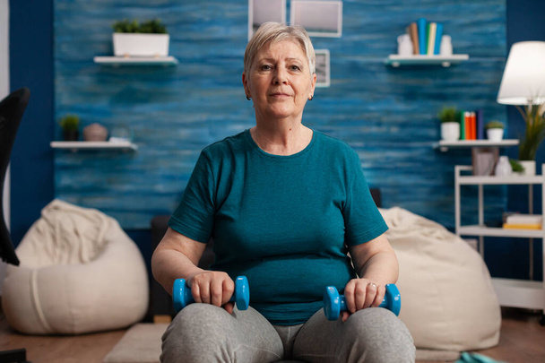Ritratto di donna anziana che guarda nella macchina fotografica mentre si siede sui muscoli del corpo dell'allenamento con la palla svizzera - Foto, immagini