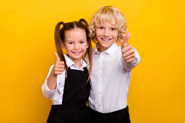 Photo of two reliable schoolkids raise thumb up approve wear school uniform isolated yellow color background - Foto, Imagem