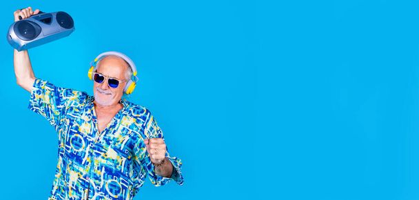 Älterer Mann tanzt Clubbing mit Boombox und drahtlosen Kopfhörern Spaß im Urlaub isoliert auf Werbe-Copyspace Hintergrund - Foto, Bild