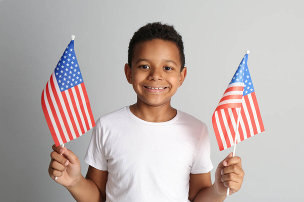 Happy African-American boy holding national flags on light grey background - Фото, изображение