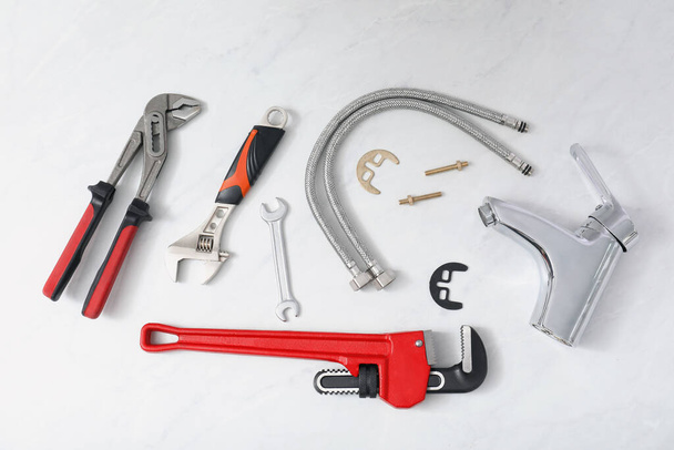 Parts of water tap and wrenches on white marble countertop, flat lay - Фото, изображение