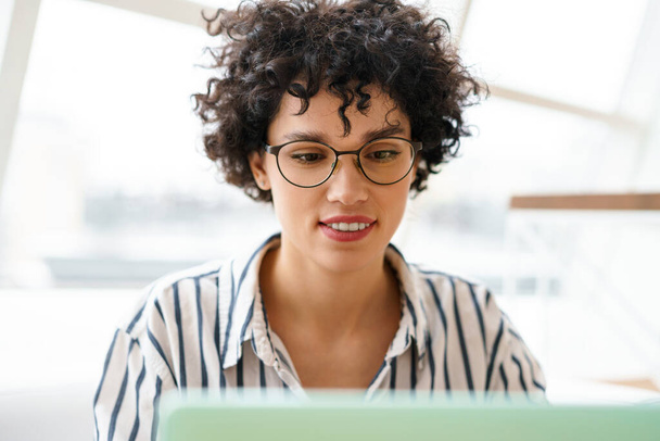 Beautiful happy woman in eyeglasses using laptop while working in cafe - Fotó, kép