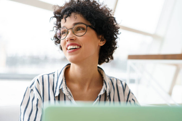 Gyönyörű boldog nő szemüvegben mosolyog, miközben dolgozik laptop kávézóban - Fotó, kép