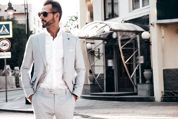 Portrait of handsome confident stylish hipster lambersexual model.Modern man dressed in elegant white suit. Fashion male posing in the street background in Europe city at sunset. In sunglasses - Fotoğraf, Görsel