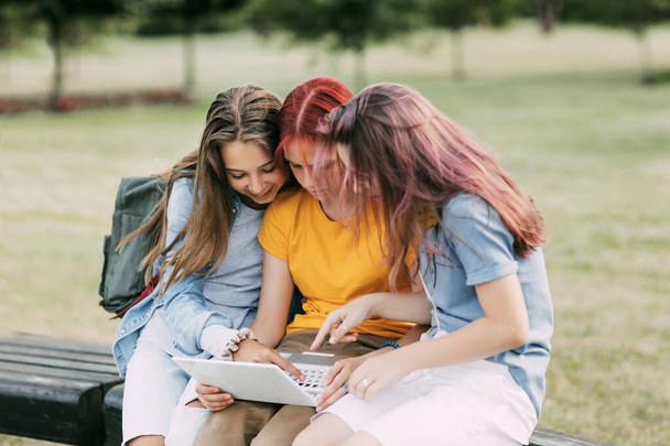 A group of teenage girls is sitting on a park bench and preparing for classes together, discussing homework and having fun. Time together, friends, friendship, training - Fotó, kép