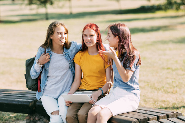 Een groep tienermeisjes zit op een bankje in het park en bereidt zich samen voor op lessen, discussieert over huiswerk en heeft plezier. Tijd samen, vrienden, vriendschap, training. - Foto, afbeelding