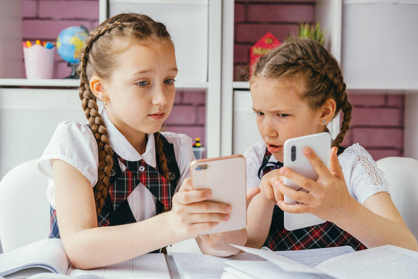 Kaksi nuorta naispuolista luokkatoveria istuu pöydän ääressä ja käyttää älypuhelimia. Modernin teknologian käsite. - Valokuva, kuva